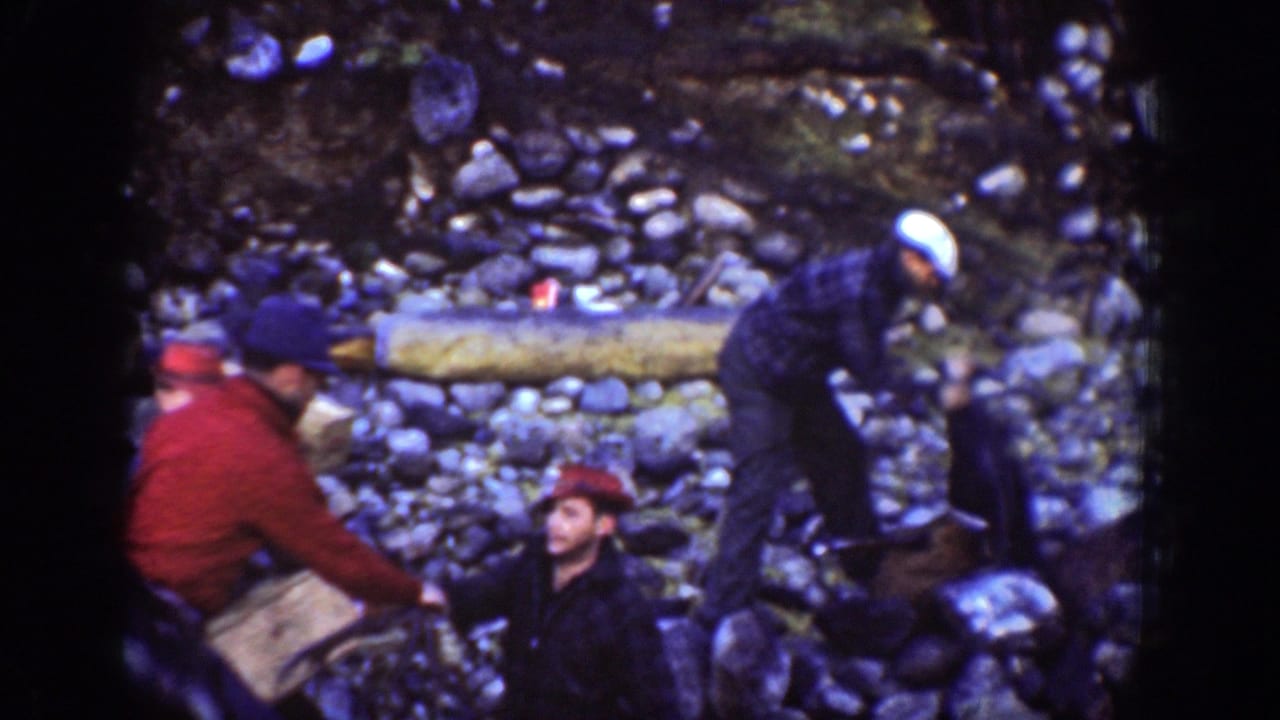 A 1939 Chelan forest work scene shows men in hats, including one in a red jacket, gathered around rocky ground and gear.