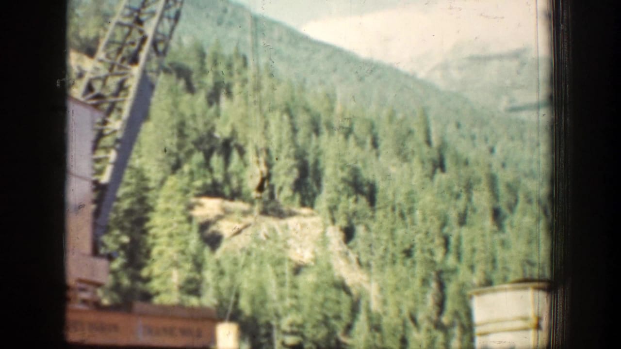 1939 Chelan-area 8mm frame showing pine-covered slopes, a partial lattice boom, and foreground window or film-frame borders.