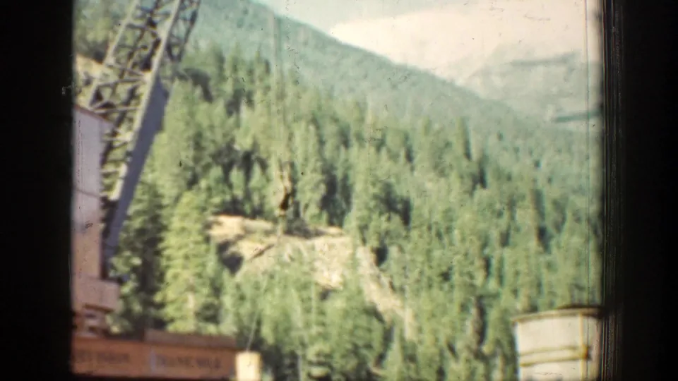 1939 Chelan-area 8mm frame showing pine-covered slopes, a partial lattice boom, and foreground window or film-frame borders.