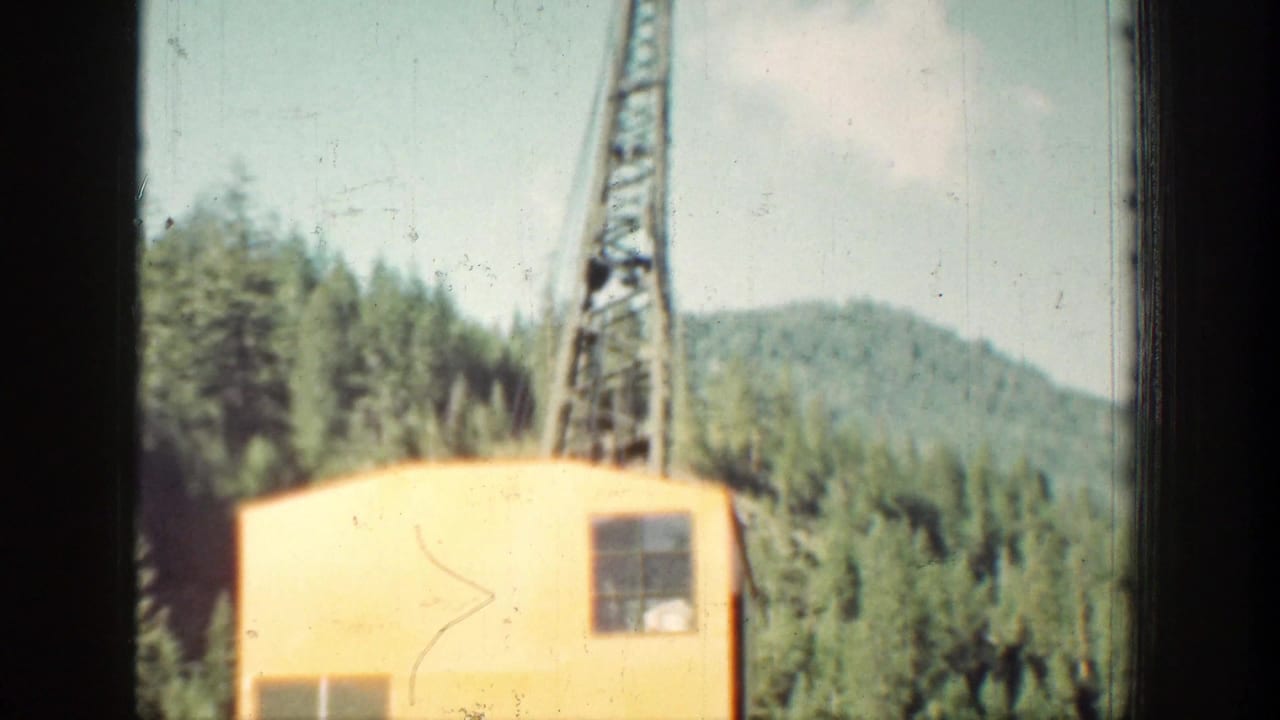 1939 Chelan, Washington footage frame with a yellow control cabin, lattice tower, forested hills, and soft faded 8mm color.