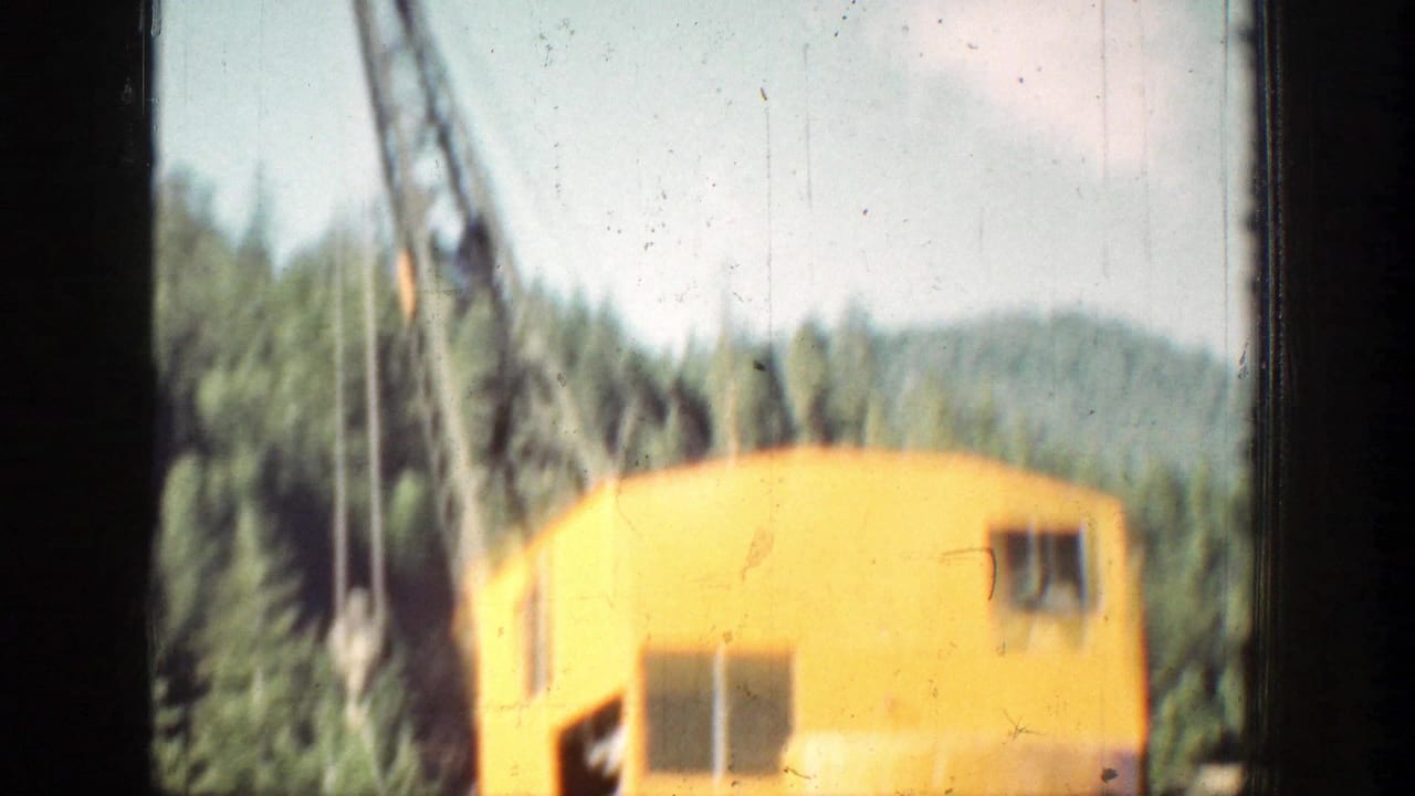 Faded 8mm frame from 1939 Chelan showing a yellow work cabin, hanging lines, boom structure, and wooded mountain background.