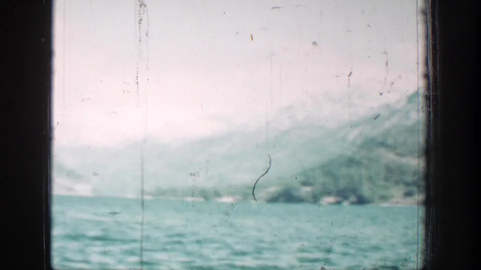 Soft 8mm view of turquoise lake water and pale, snow-dusted mountain slopes near Chelan, Washington.