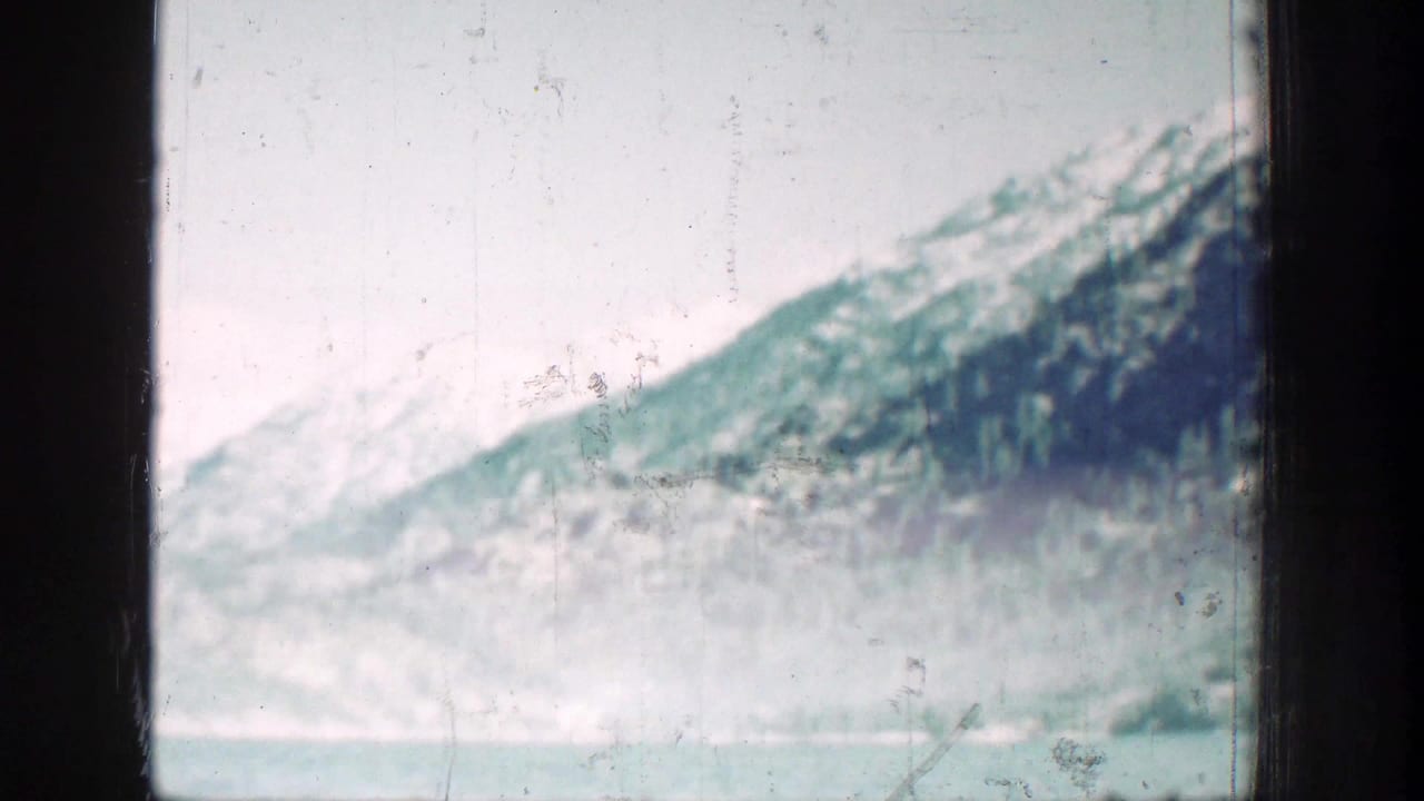 Chelan-area mountain lake scenery with pale water, snowy slopes, forested hillside, and heavy home-movie film texture.