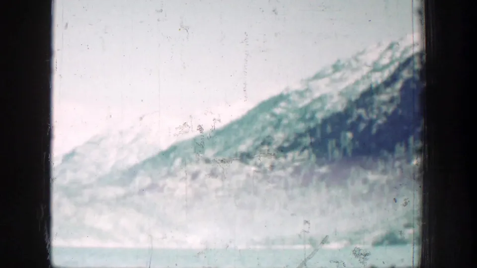 Chelan-area mountain lake scenery with pale water, snowy slopes, forested hillside, and heavy home-movie film texture.