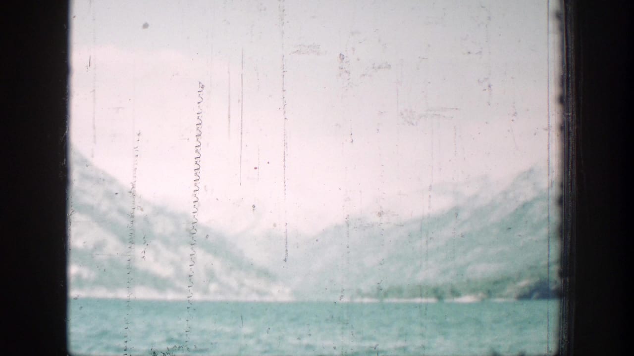 Mountain lake with pale sky and distant slopes seen through scratched 8mm film.