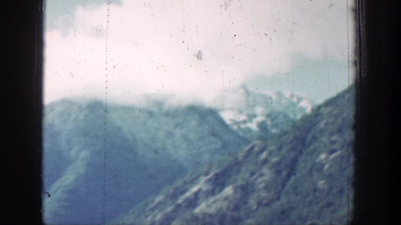 A soft 1939 8mm view of Chelan mountain slopes and lake water, with haze, faded color, and vertical film wear.
