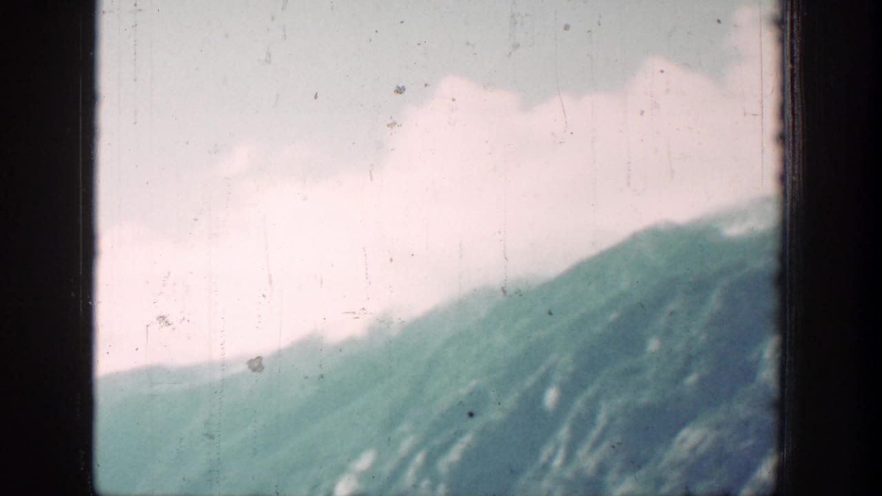 Soft 8mm mountain landscape near Chelan, Washington, with green slopes, pale clouds, and visible film wear.
