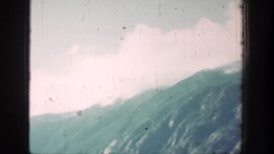 Soft 8mm mountain landscape near Chelan, Washington, with green slopes, pale clouds, and visible film wear.