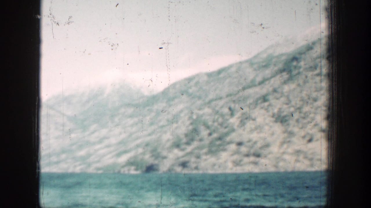 1939 home-movie view across Lake Chelan toward a steep mountain shoreline, with soft exposure and visible film scratches.
