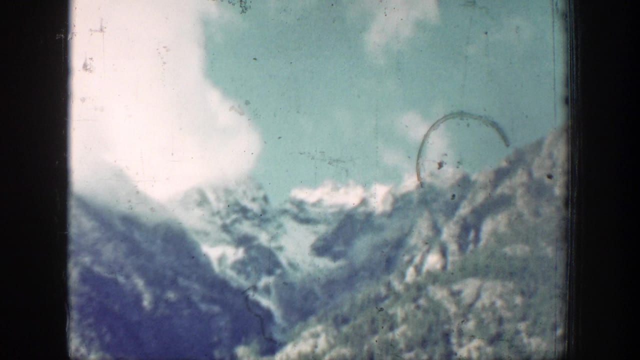 Snowy mountain peaks and forested slopes seen through dark window framing.