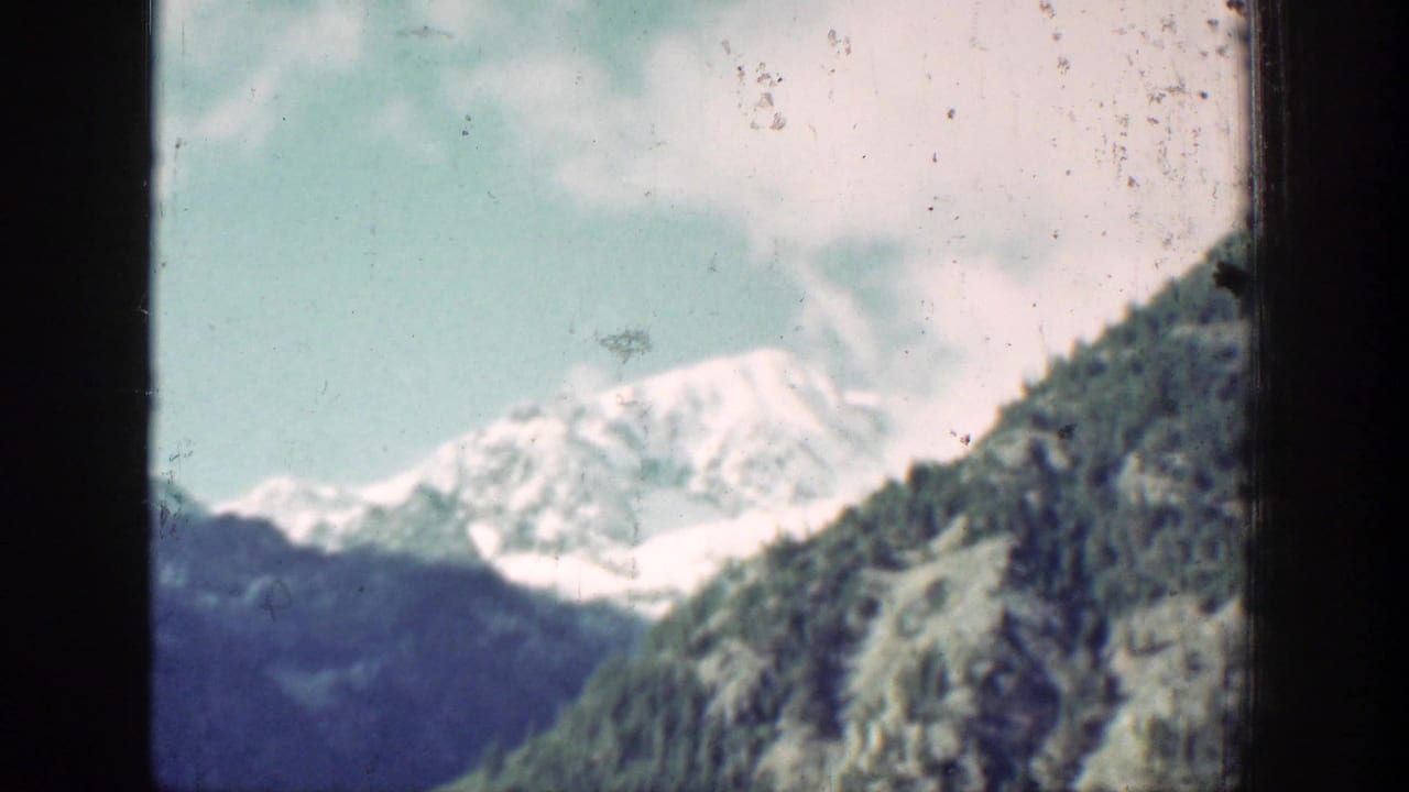 1939 8mm view of Chelan-area mountain terrain, with a snow-covered peak and green wooded slope through window framing.