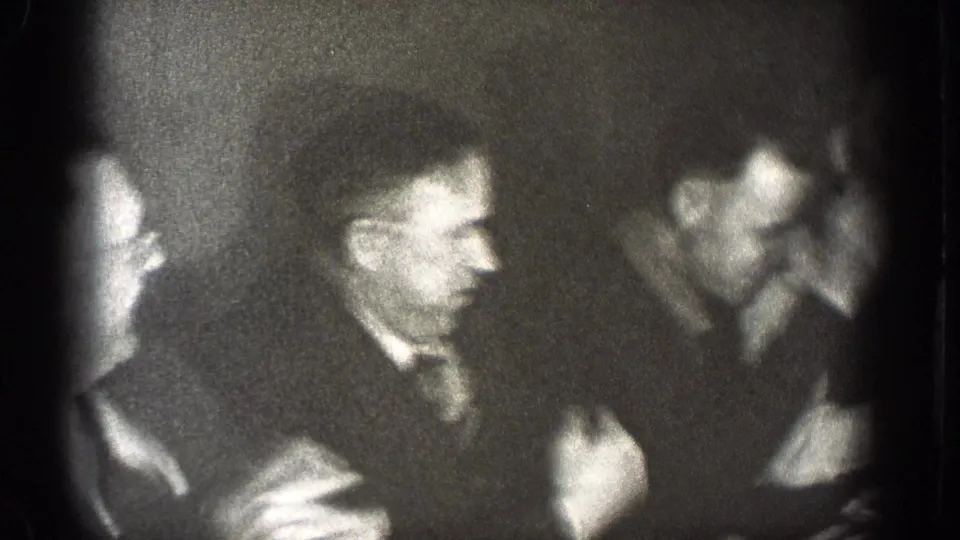 Grainy 1939 Chelan, Washington frame of men in suits laughing and talking during an indoor formal gathering.