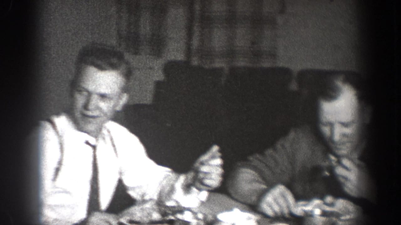 Two men seated at a table during a meal, one in a white shirt and tie gesturing.