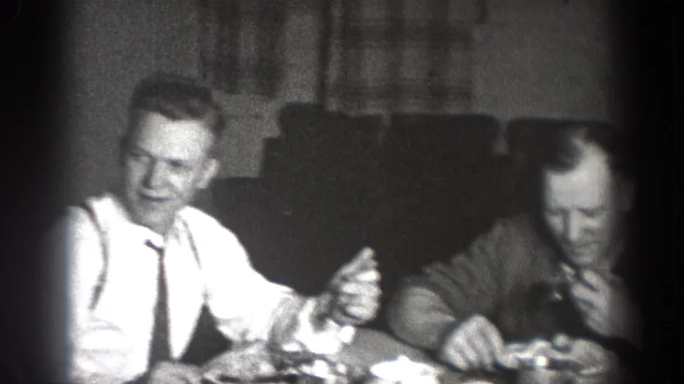 1939 Chelan, Washington home-movie frame of men seated at lunch, with one man in a white shirt and tie gesturing at the table.