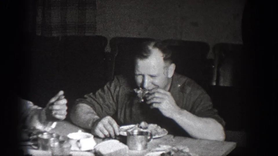 1939 Chelan, Washington home-movie frame showing a man in a dark shirt eating at a lunch table in a dim interior.