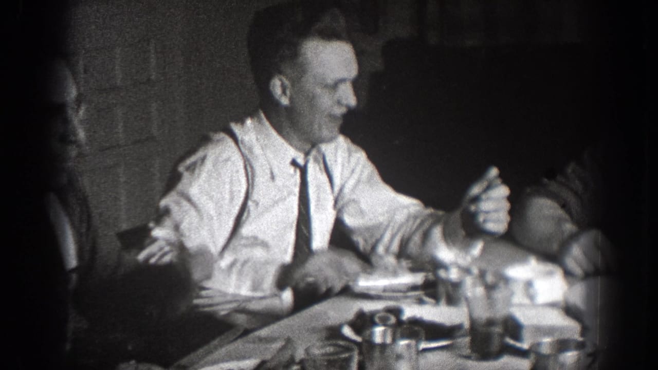 1939 Chelan, Washington home-movie frame showing a smiling man in a white shirt and tie at a shared lunch table.