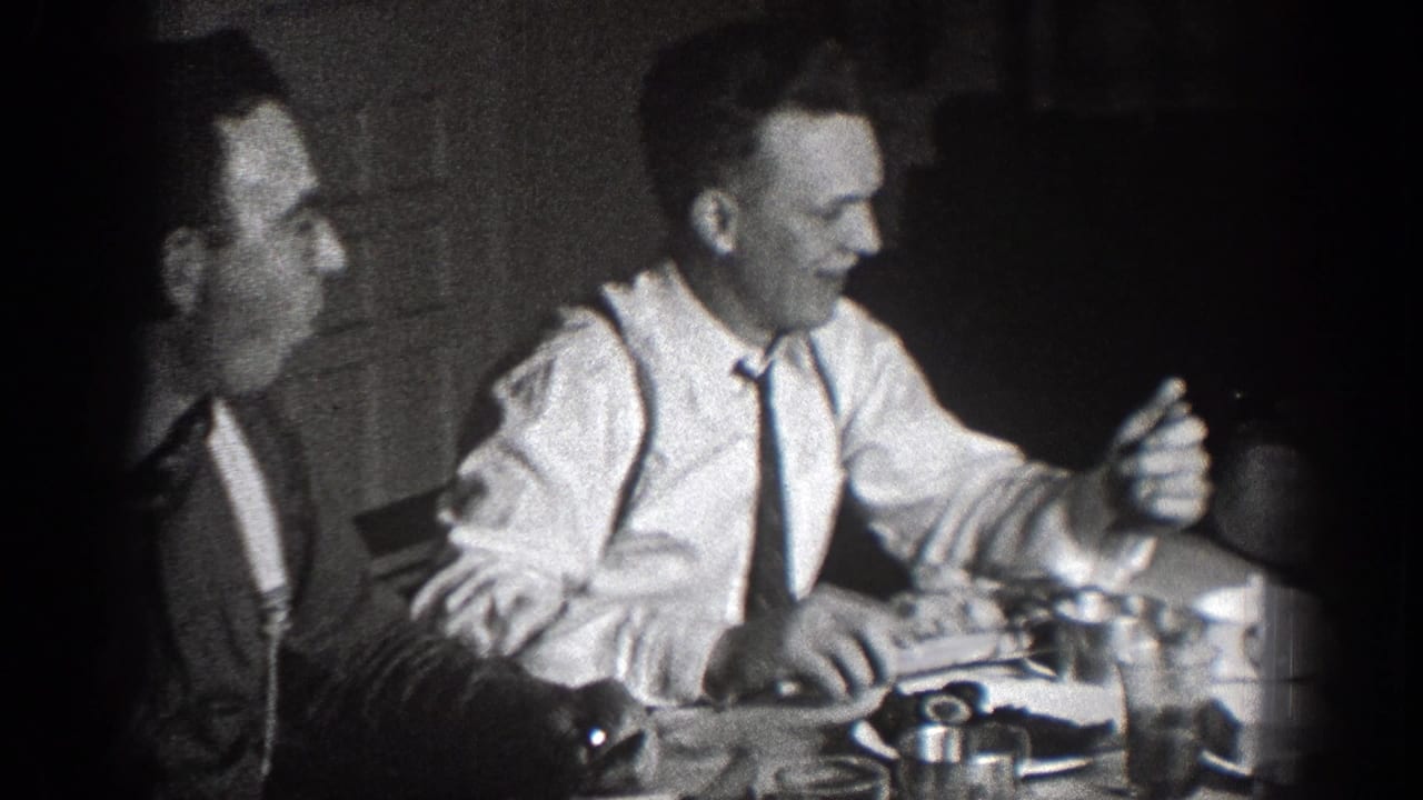 Two seated men in ties sit at a dining table with plates and cups.