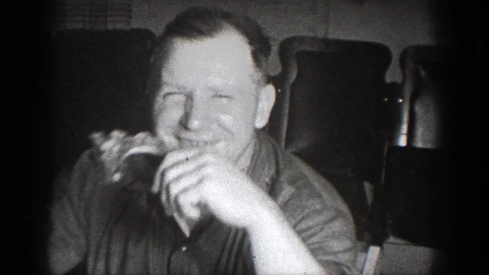 A man smiles while eating in a black-and-white 8mm frame from the 1939 Chelan, Washington gathering.