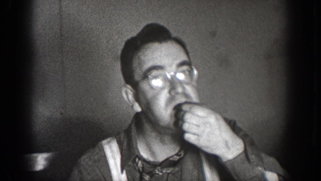 A man wearing glasses eats in a close interior frame from the 1939 Chelan, Washington home-movie footage.