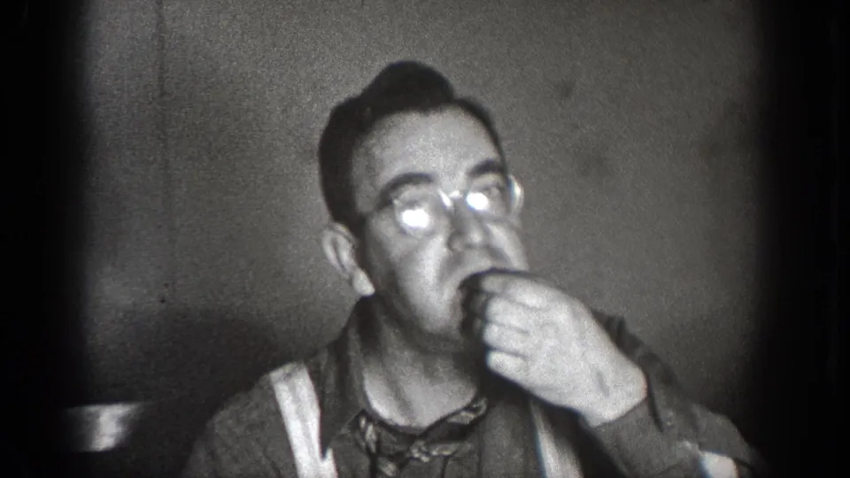 A man wearing glasses eats in a close interior frame from the 1939 Chelan, Washington home-movie footage.