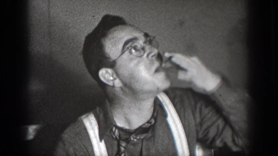 In 1939 Chelan, Washington home-movie footage, a man in glasses and suspenders raises food to his mouth at an indoor meal.