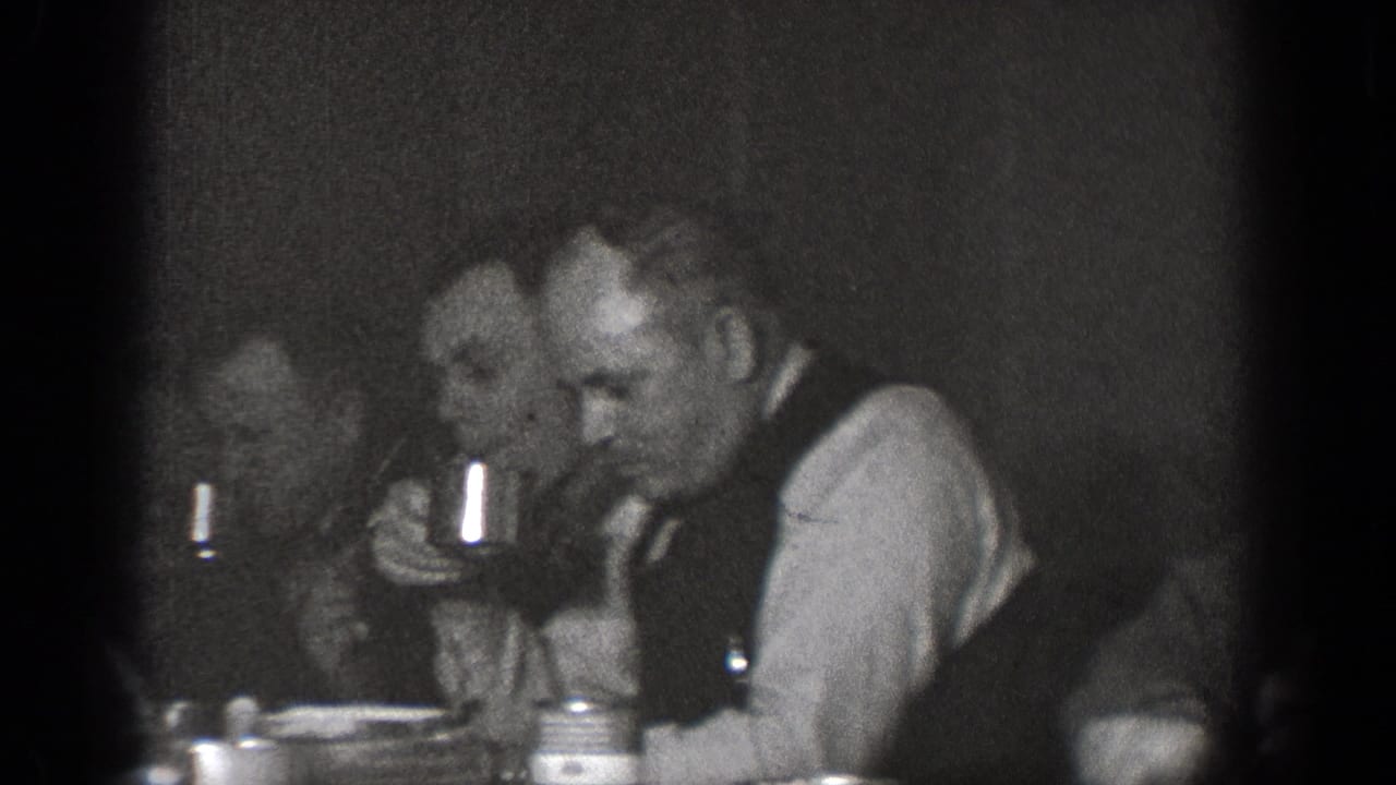 Several adult men sit close together at an indoor table, eating and drinking from cups in 1939 Chelan, Washington home-movie footage.