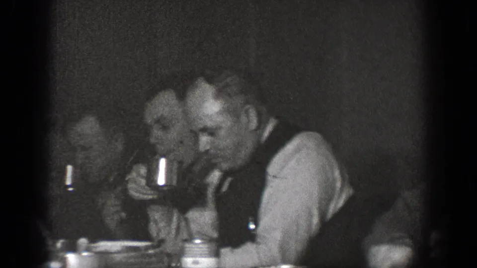 Several adult men sit close together at an indoor table, eating and drinking from cups in 1939 Chelan, Washington home-movie footage.