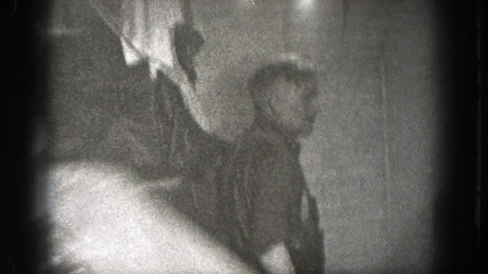 A soft-focus frame shows a seated man near a cup during the indoor meal, with the 8mm image blurred by motion and exposure.