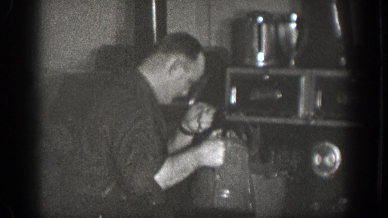In 1939 Chelan, Washington home-movie footage, a man bends over a stove while working with a kettle and pot in a dark kitchen.