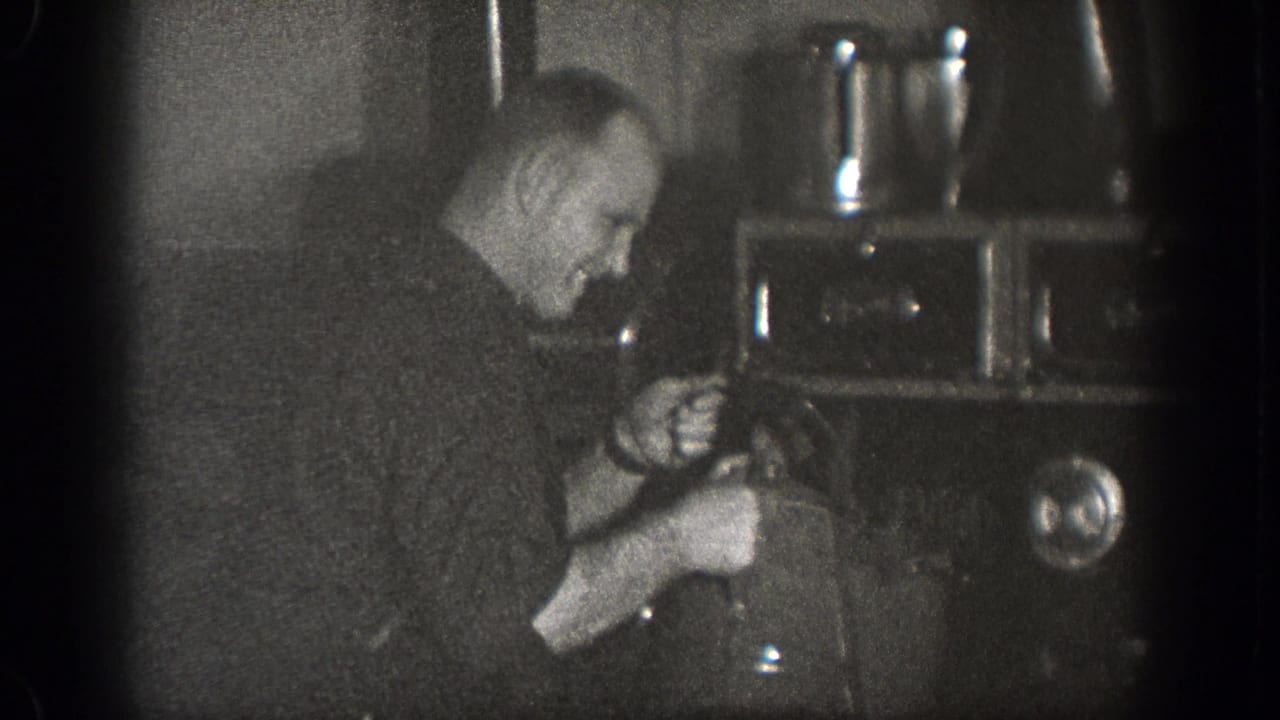 A man in a dark shirt appears to pour or handle liquid from a kettle into a pot on a stove in a 1939 Chelan kitchen scene.