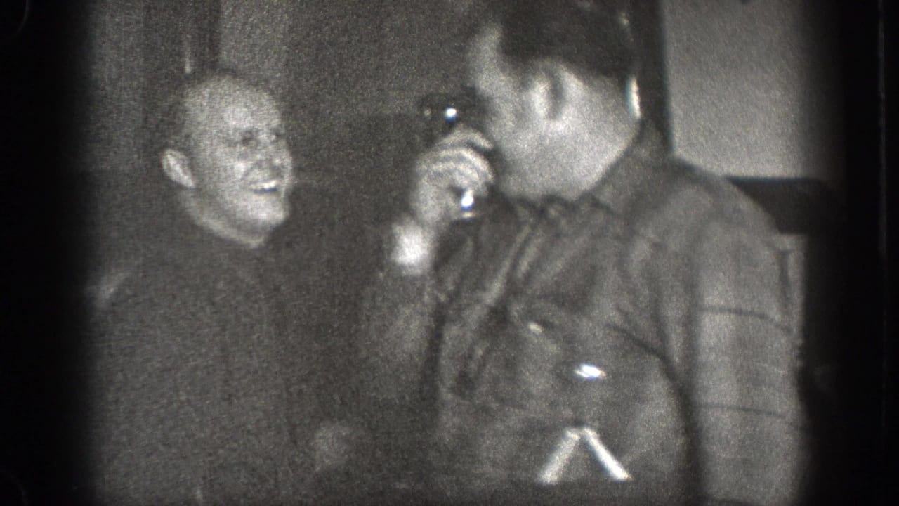 Two adult men appear to share a light moment inside the 1939 Chelan kitchen, with one holding a small cup or vessel near his face.