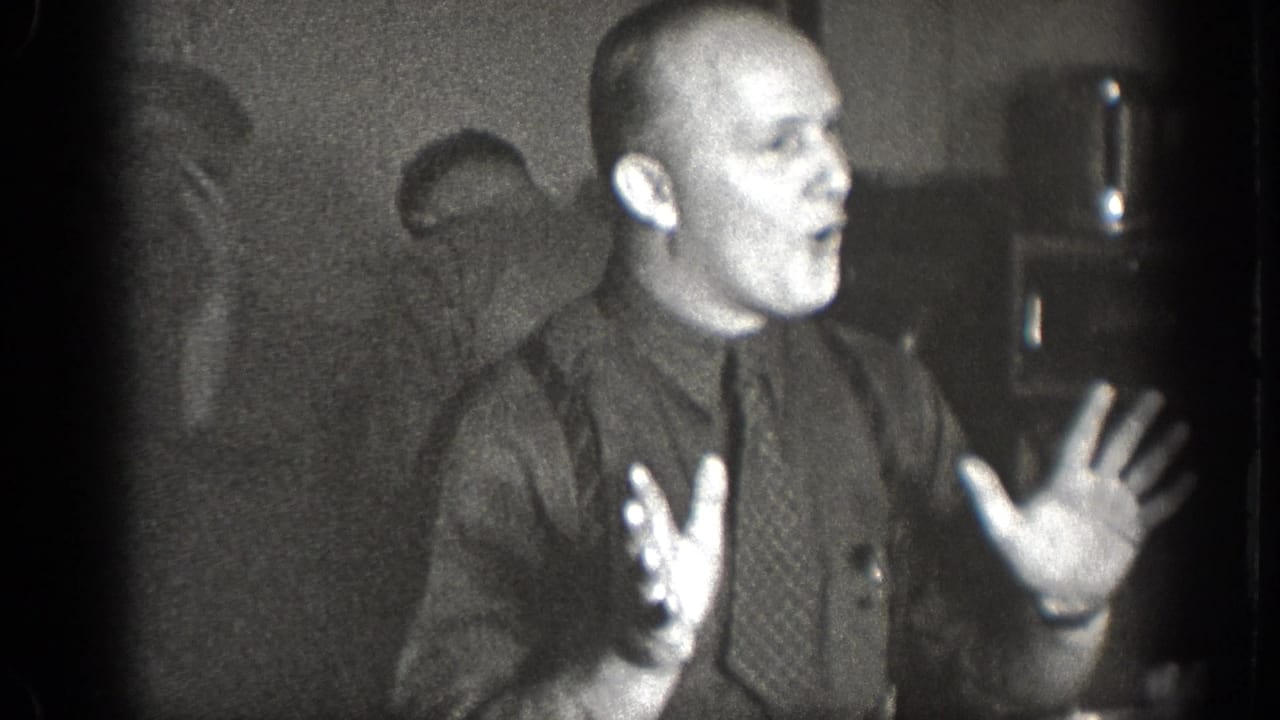 In the final 1939 Chelan frame, a man in a dark shirt and tie raises both hands while speaking or laughing among other men indoors.