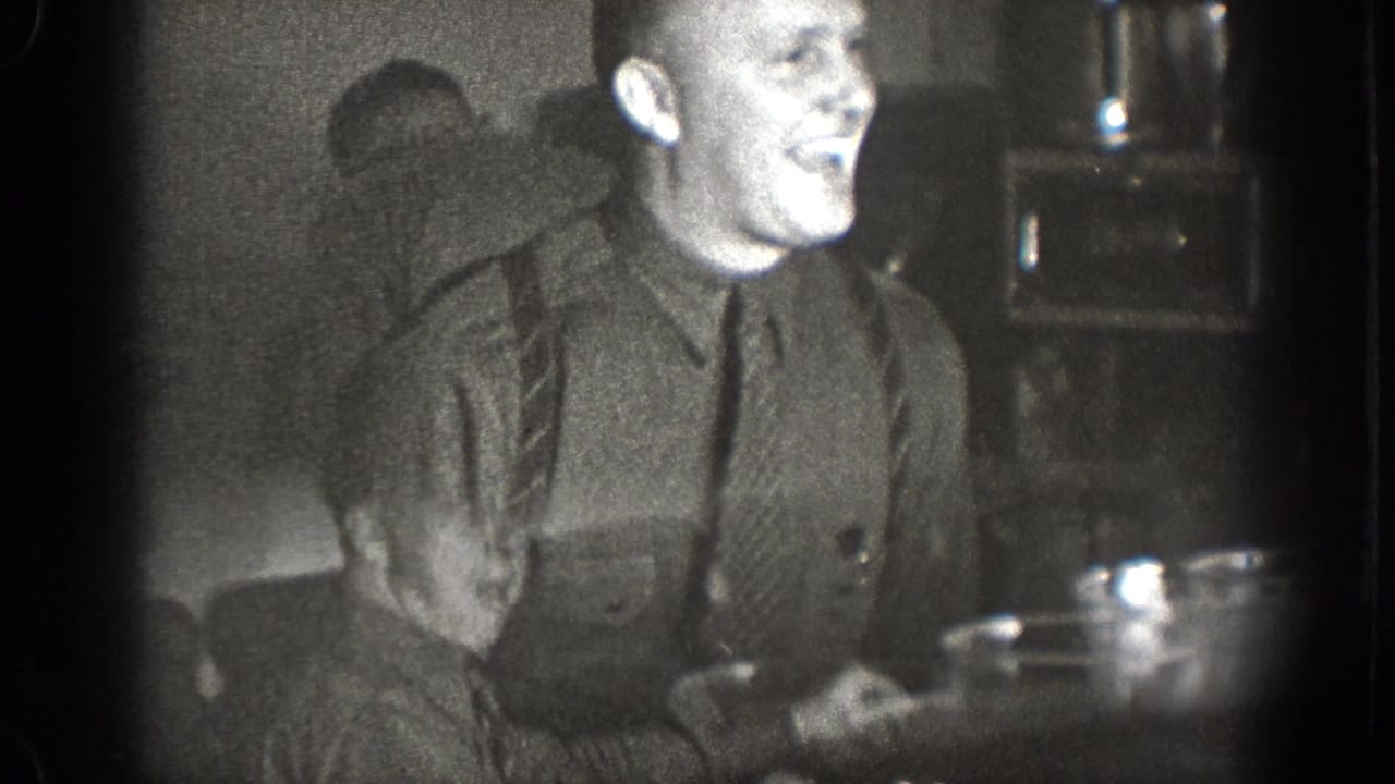 Man in a dark sweater seated at a table in a dim interior, gesturing while eating.