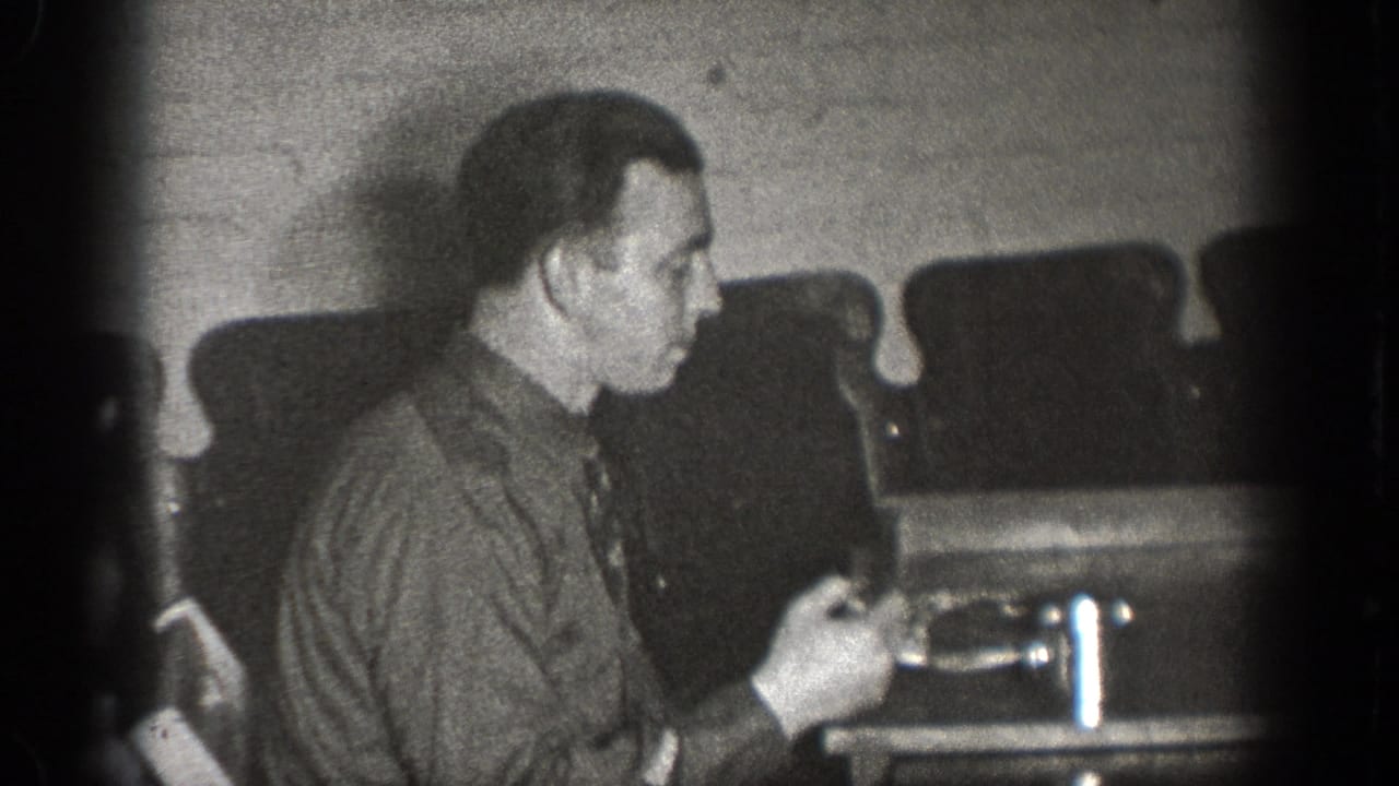 A man sits in profile at a lunch table in the Chelan, Washington home movie, with cups and upholstered seating behind him.