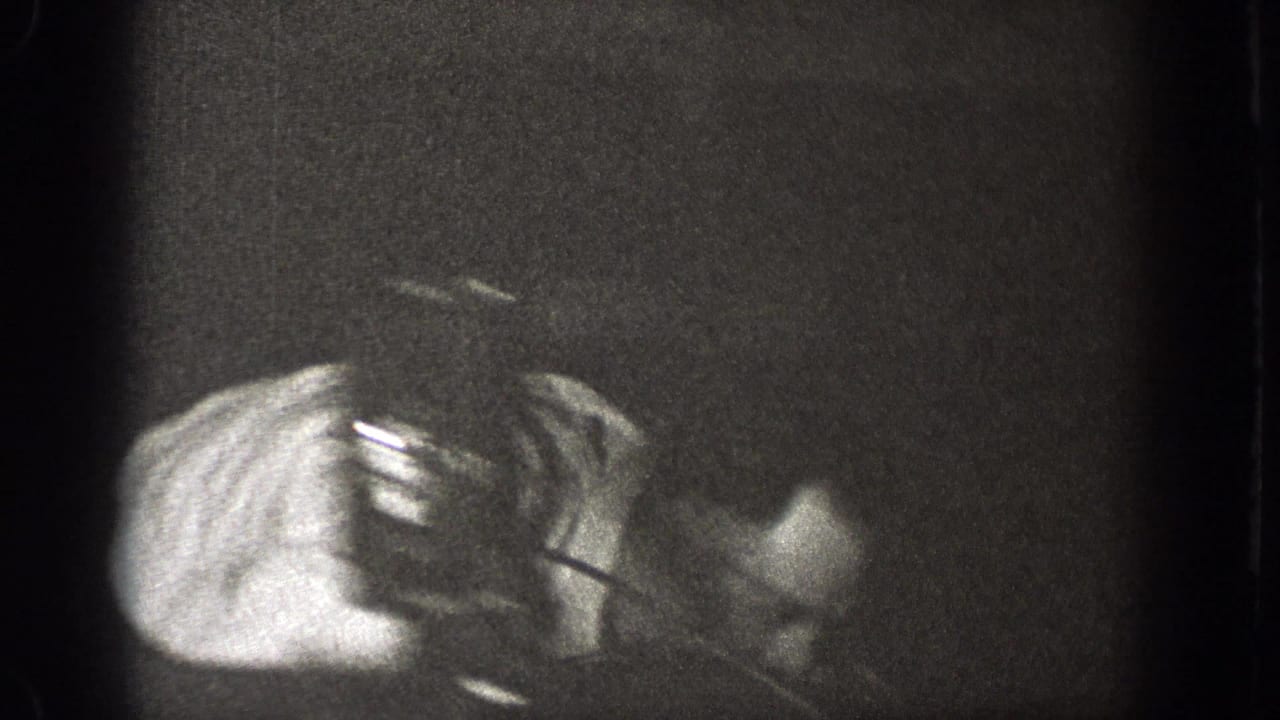 A mostly obscured 8mm frame from the indoor gathering shows a partial arm and hand, with little room detail visible.