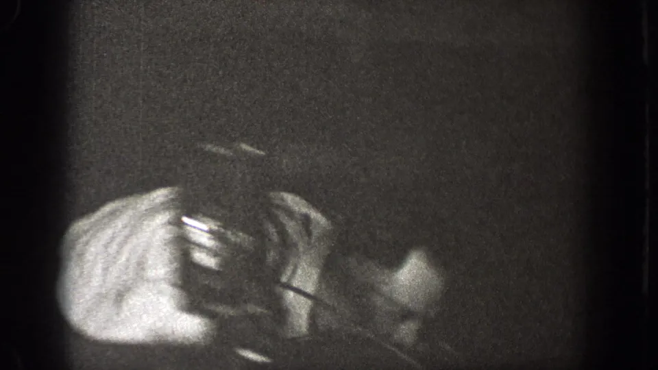 A mostly obscured 8mm frame from the indoor gathering shows a partial arm and hand, with little room detail visible.