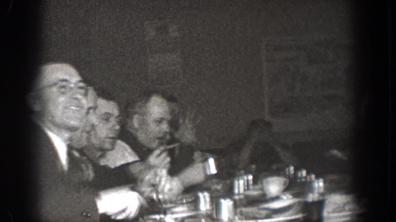 In a 1939 Chelan, Washington home-movie frame, several suited men sit close together at a dim dinner table.