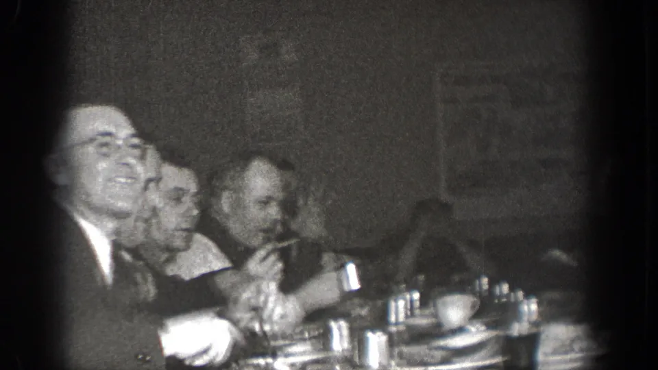 In a 1939 Chelan, Washington home-movie frame, several suited men sit close together at a dim dinner table.