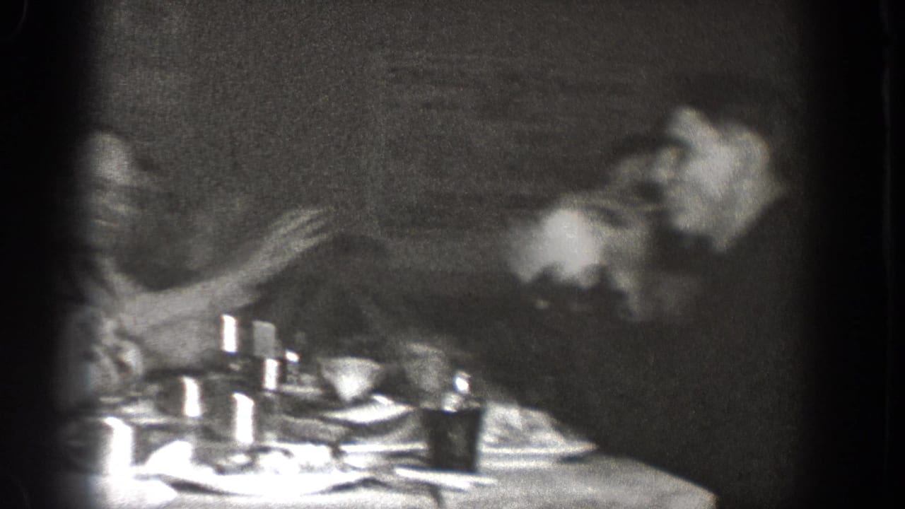 Motion blur obscures part of the 1939 Chelan dinner frame, but a seated man and table setting remain visible.
