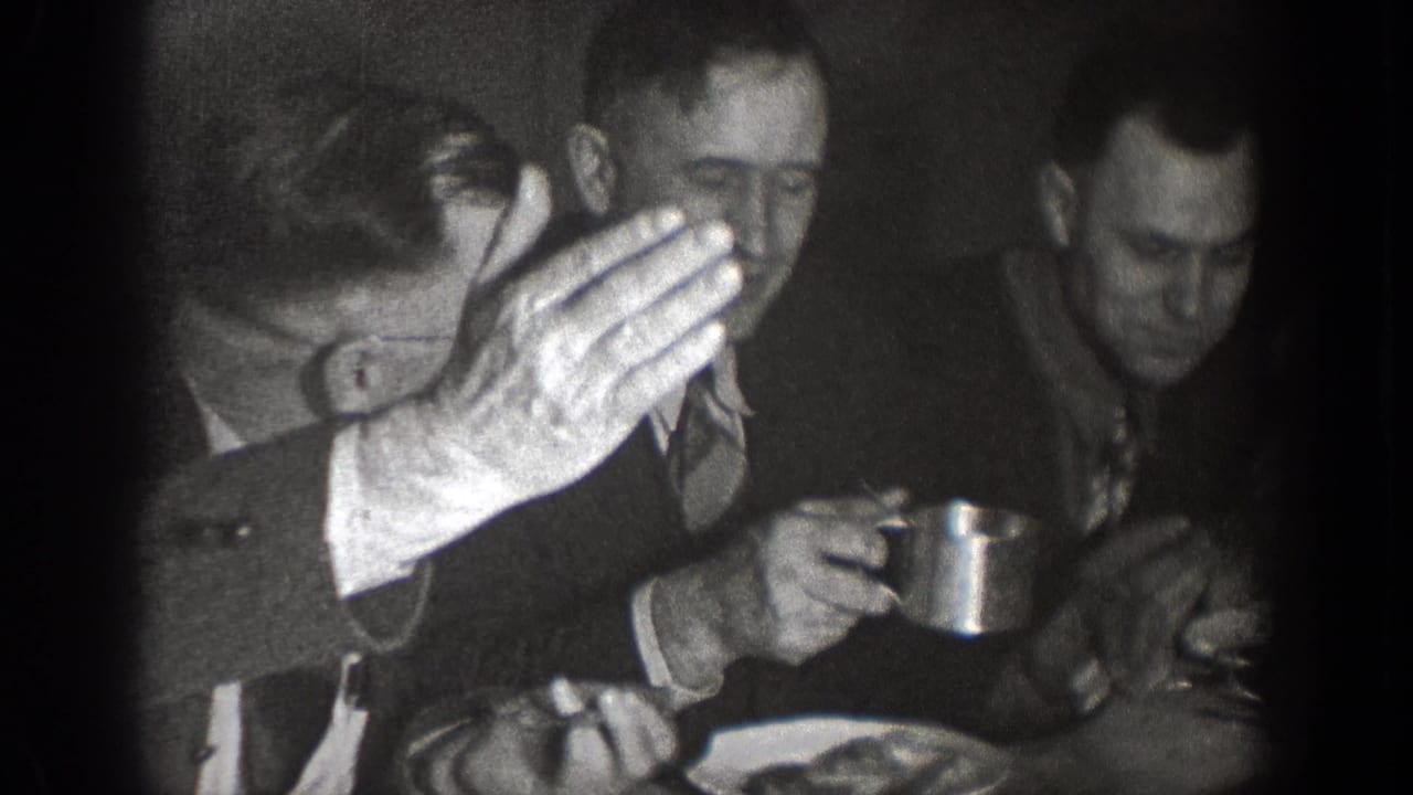 Three men seated at a table, one partly covering his face while another holds a cup.