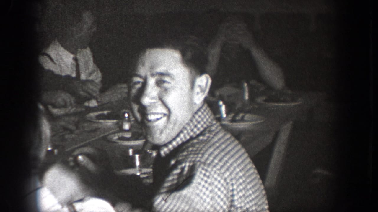 A man smiles toward the camera during the Chelan, Washington indoor gathering, with other diners and tableware around him.