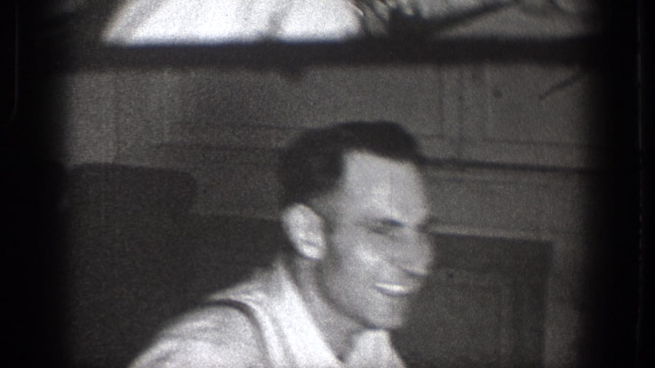 Smiling adult man in close-up, filmed indoors on black-and-white 8mm footage from Chelan, Washington.