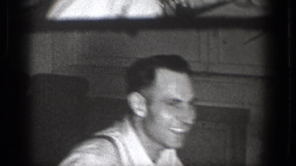 Smiling adult man in close-up, filmed indoors on black-and-white 8mm footage from Chelan, Washington.