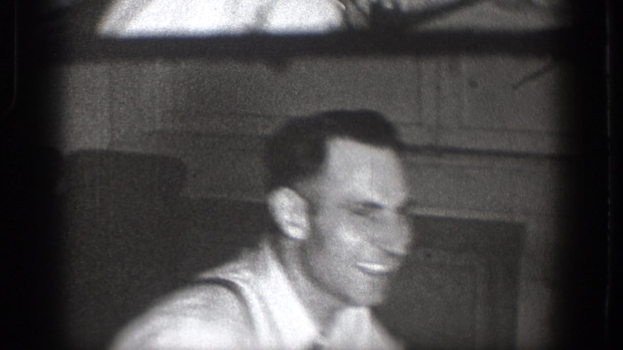 Close-up of the smiling man in a white shirt, with a paneled interior wall behind him.