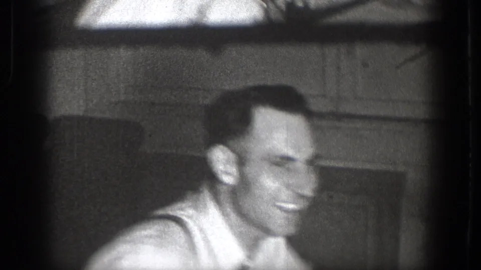 Close-up of the smiling man in a white shirt, with a paneled interior wall behind him.
