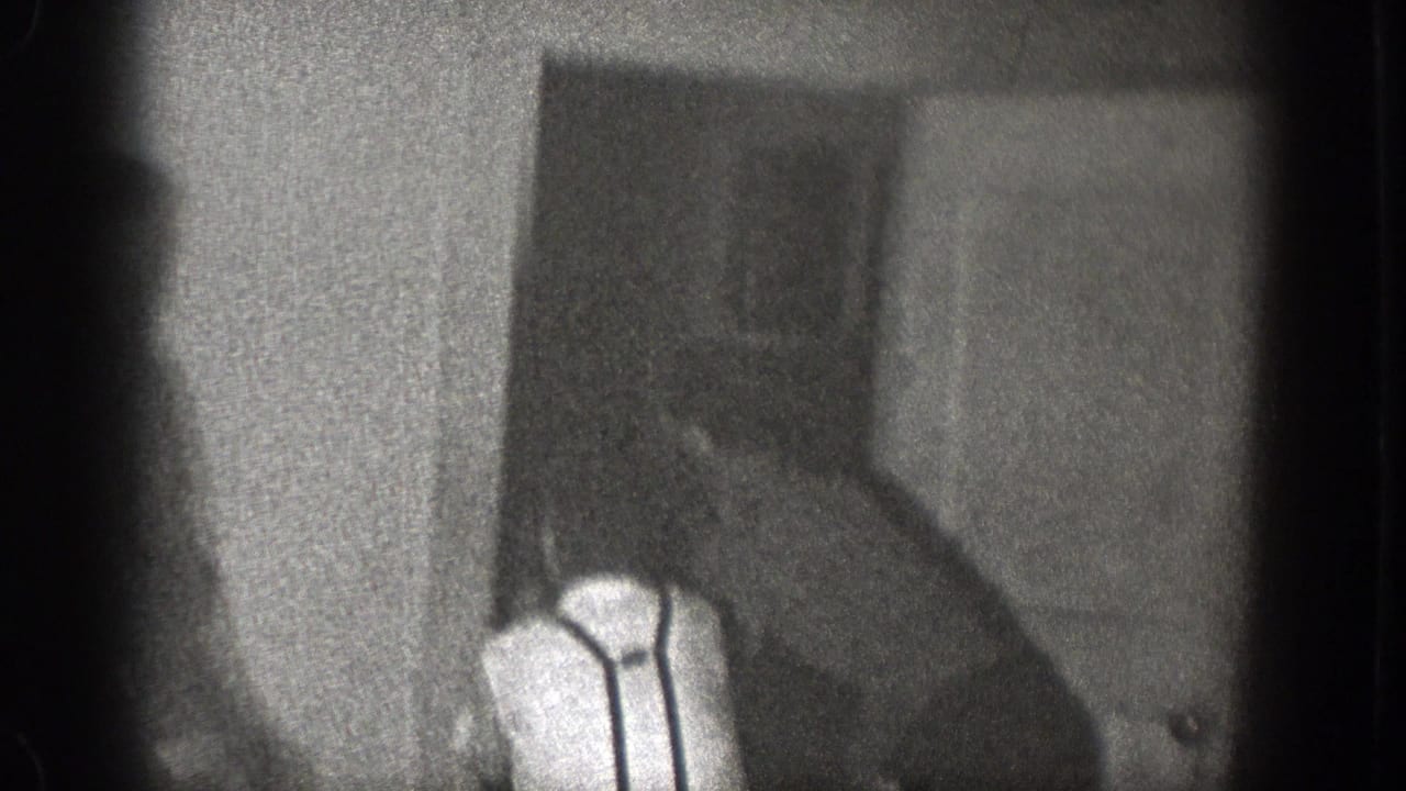 1939 Chelan, Washington home-movie frame showing a man in a white shirt and suspenders near a door in a dim private room.