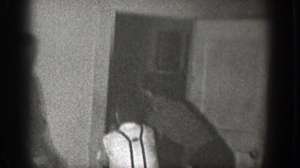 1939 Chelan, Washington home-movie frame showing a man in a white shirt and suspenders near a door in a dim private room.