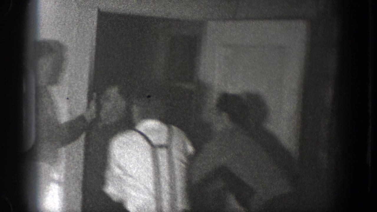 Men gather and begin to press together near a doorway in this grainy 1939 Chelan interior home-movie frame.
