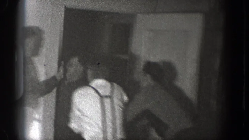 Men gather and begin to press together near a doorway in this grainy 1939 Chelan interior home-movie frame.