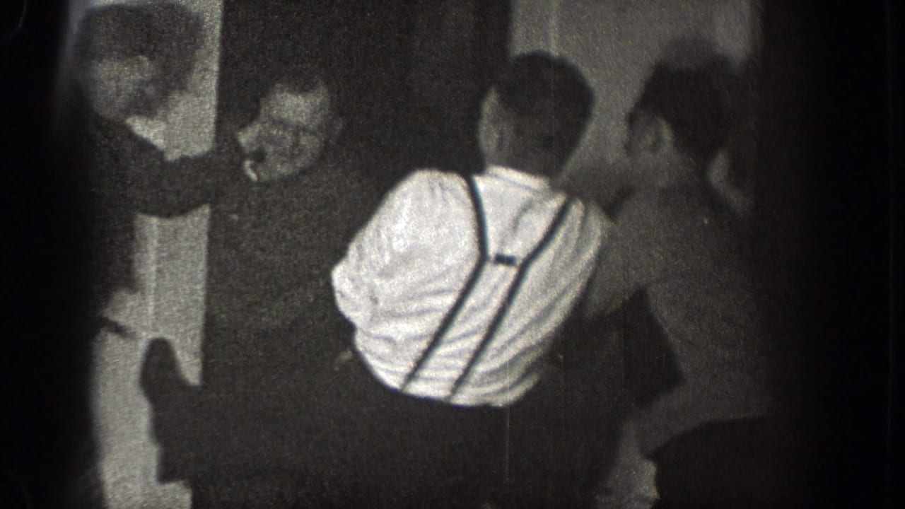 In a Chelan, Washington interior, several adult men appear to grapple near a door as the home-movie camera records from close range.